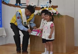 片桐西幼稚園の壇上で女子園児の2人が警察官の方にプレゼントを渡している写真