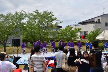 屋外ステージで紫の衣装でジャグリングショーをする団体と来場者たちの写真