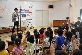郡山西幼稚園で行われた演奏会でウクレレを演奏する鈴木智貴氏と演奏を楽しんでいる園児たちの写真