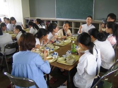 テーブルを囲んで給食を食べている様子の中国の中学生たちと日本の小学生たちの写真