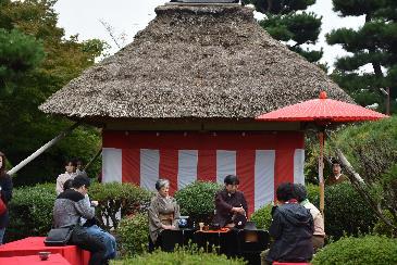 茅葺屋根のある、立派な庭園で茶道を楽しむ人達の写真