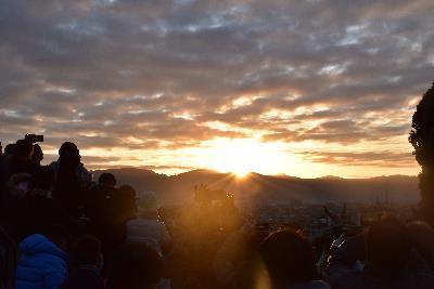 雲と山の間から日の出が現れる様子を眺める登山者達の写真