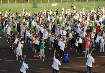 屋外で参加者たちが片手を上げて体操をしている写真