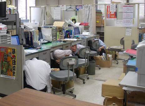 地震発生の防災訓練で、急いで机の下のもぐる職員たちの写真