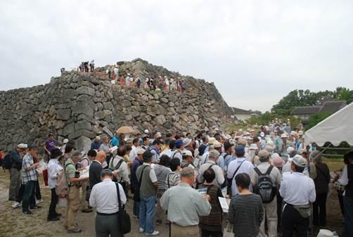 積み上げられた石垣の土台の上に登っている人たちや、資料を見ながら集まっている人たちの写真