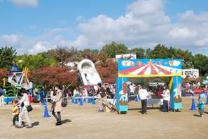 公園の広場に、遊園地の様な仮設のゲートが作られ、中に様々な遊具が備え付けられた様子の写真