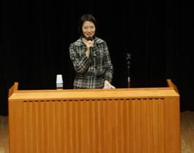 緑色のチェックの服装をした女性が登壇して、講演を開いている様子の写真