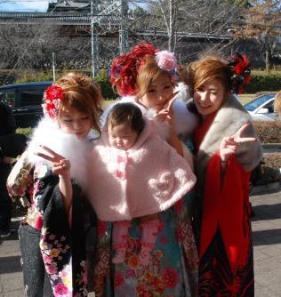 成人式の会場の外で赤ちゃんを抱きかかえながらピースサインをする振り袖姿の女性と2人の振り袖姿の女性の集合写真