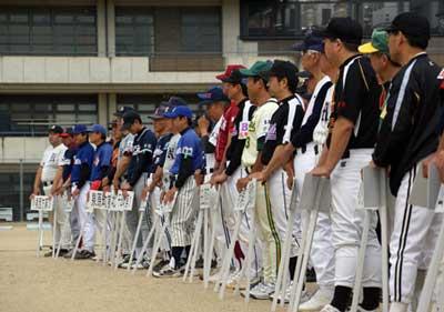 運動場で列の先頭のソフトボール大会の選手の男性たちがチーム名の書かれたプラカードを手にして横に並んでいる写真