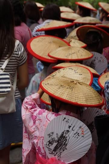 境内で着物を着て三度傘を被った女性や祭りの来場者たちが密集している写真