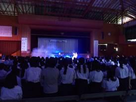 青紫色のライトで照らされた舞台を立って注目している多くの中学生の後ろ姿の写真