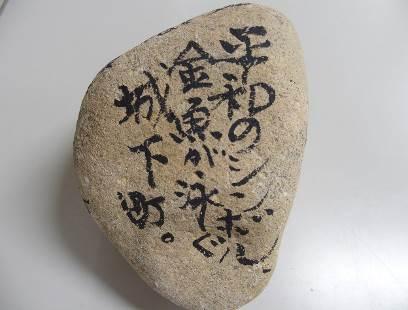白い机に置かれた「平和のシンボル金魚が泳ぐ城下街。」と書かれた石の写真