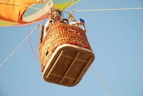青空に浮かぶロープの張られたかごに人が乗っている気球を下から見上げた視点の写真