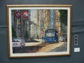 木製の額縁に入った自動車と青い路面電車が行きかう街中の風景の油絵が置かれている写真