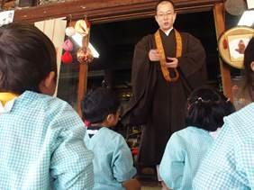 お寺の室内で水色のスモックを着た園児たちを前に立つ袈裟を着た男性の写真