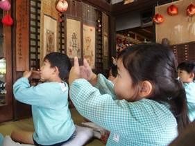 お寺の室内で水色のスモックを着た園児たちが座布団の上で座禅を組み両手の指を重ねている写真