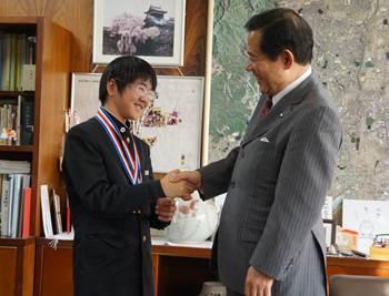 市長室で金メダルを2つ首からかけた男子中学生と握手をしている市長の写真
