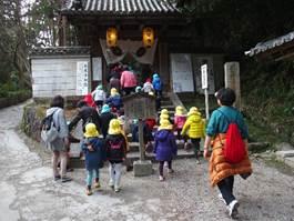黄色い帽子を被った園児たちが、お寺の門をくぐっている様子の写真