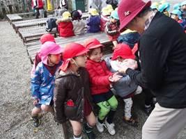 赤い帽子を被った年配の女性から園児が飴を貰っている様子の写真