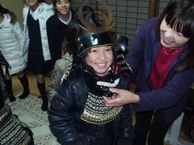 講師に黒い甲冑を付けてもらって、笑みを浮かべる子供の写真
