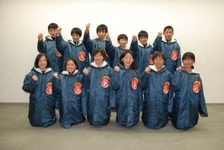 ガッツポーズをして集合写真に臨む、紺色の防寒コートを着た12名の選手たちの写真