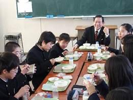 黒いスーツの男性と楽しそうに給食を食べる中学生たちの写真