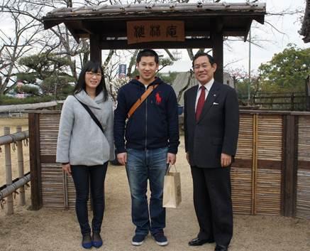 木と竹で作られた門の前で、スーツ姿の男性から記念品を受け取っているカップルの写真