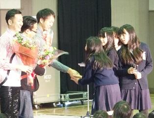 3人の花束を持った男性が4人の女生徒と握手している処の写真