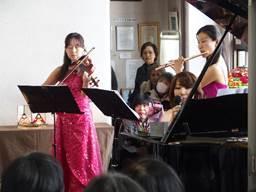 バイオリンとフルートを演奏するピンクのドレスを着た2人の女性の写真