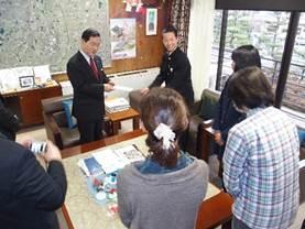 執務室で、市長に義援金手渡す男性と職員の写真