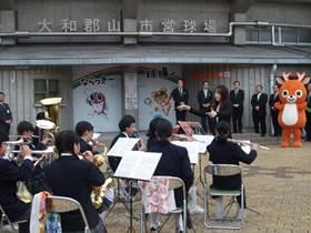 「大和郡山市営球場球場」のロゴがある入り口を前にして、吹奏楽部の生徒が演奏している処の写真