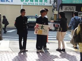 横断歩道の前で、募金活動する三人の男子生徒と募金する女性の様子