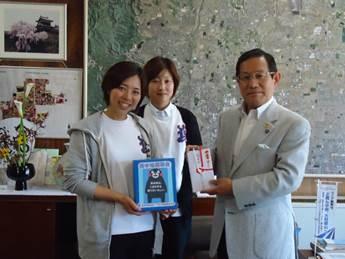 執務室で、白いユニフォームを着た二人の女性が、市長に義援金を渡した時の写真