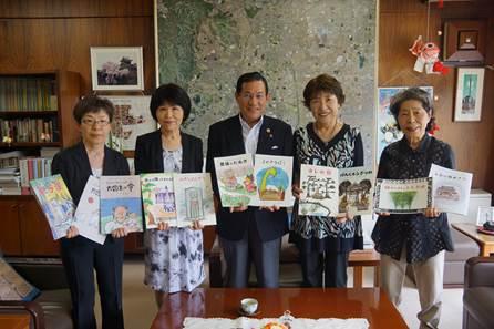 市長と両脇の4人の女性が民話や伝承が書かれた絵本を掲げている様子の写真