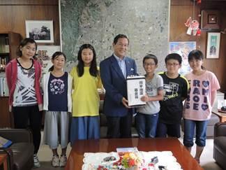 執務室で、市長に募金箱を手渡す6人の小学生たちの写真