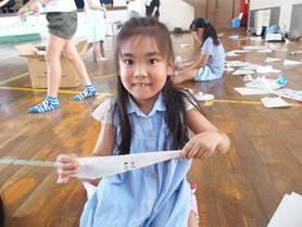 水色のワンピースを着た女の子が紙飛行機を作っている処の写真
