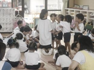 絵本の読み聞かせをするボランティアの小学生に園児たち集まってきている処の写真