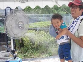 お父さんに抱えられた小さい子がミスト扇風機にあてられて笑っている様子の写真