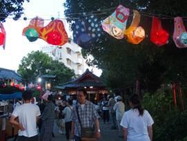 祭りに色を添える幾つもの提灯の下を歩く参拝者たちの写真