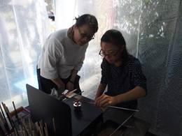 仮設テント内で作家の方がガラス細工の作成工程を説明ながら体験をしている年配の参加者の女性の写真