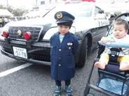「ちびっこポリス」でパトカーの前で制服を着た男の子とベビーカーに乗った幼児の写真