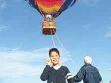 小学4年生の稲田くんが気球をバックにピースサインをしている写真