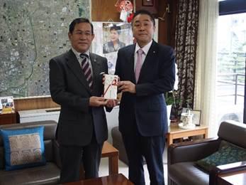 市長室で奈良県中古自動車販売商工組合の男性が市長に寄付金を渡している写真