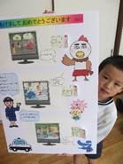鶏のマスコットの絵やお巡りさんの絵が描かれた「交通安全ジャンボ年賀状」を手に笑みを浮かべる園児の写真