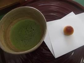 お盆に乗せられた抹茶と和紙の置かれた茶菓子の写真