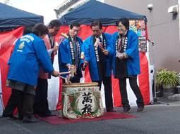 はっぴを着た市長を含む7人が一斉に大きな酒樽を割って乾杯する写真