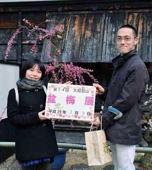 「第14回大和郡山盆梅展」と書かれたプレートを持つ夫婦の写真