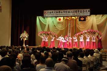 赤を基調とした衣装で、フラダンスのサークルの女性たちがステージ上で踊っている様子と、それを見ている観客の写真