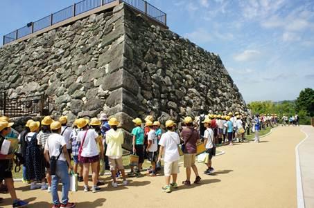 郡山城の天守台の前に集う黄色の帽子を被った小学生たちの写真