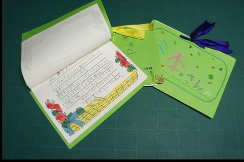 手作りの緑色の表紙にリボンで止められた、3冊の冊子と開かれている手書きの手紙の写真